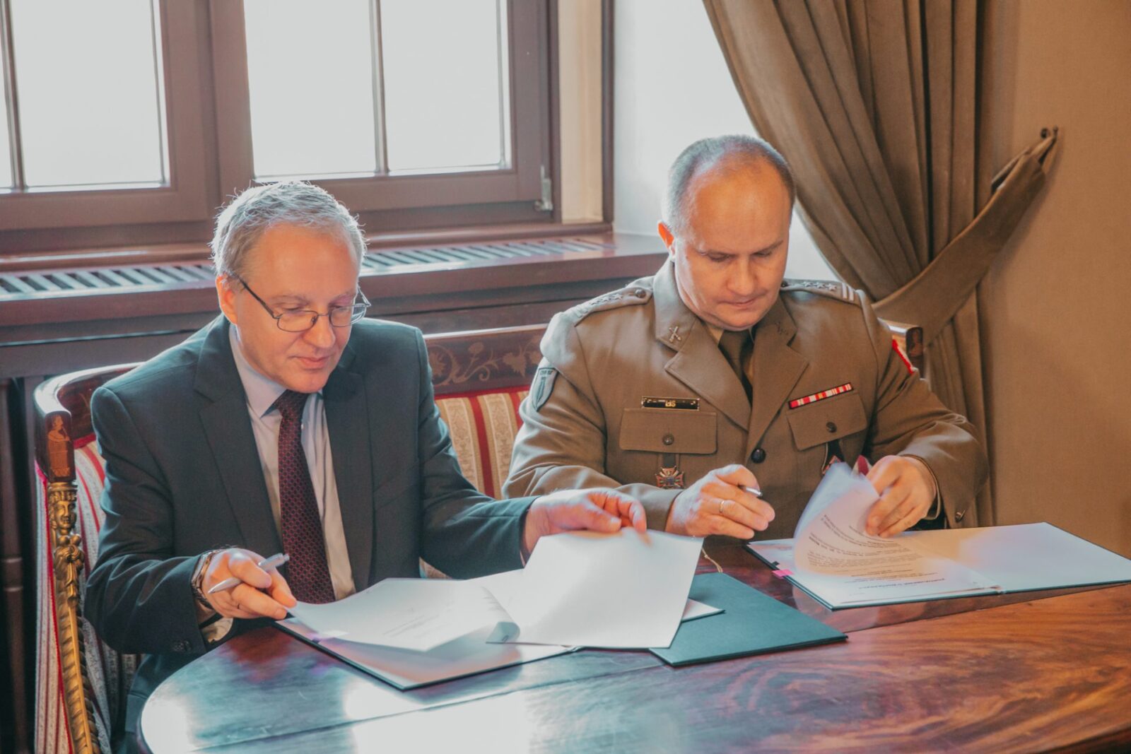 dwaj mężczyźni podpisujący dokumenty przy stole